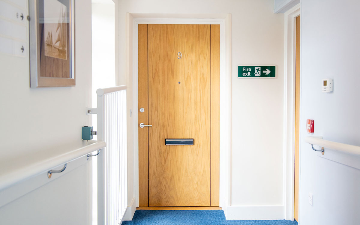 A brown fire door at the end of a hallway in a flat building.