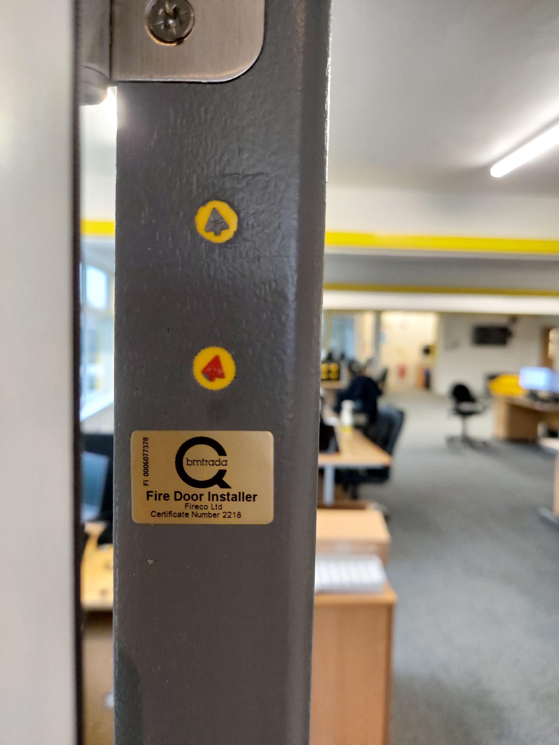 close up of a grey fire door showing 2 yellow plugs and gold sticker all showing door certification
