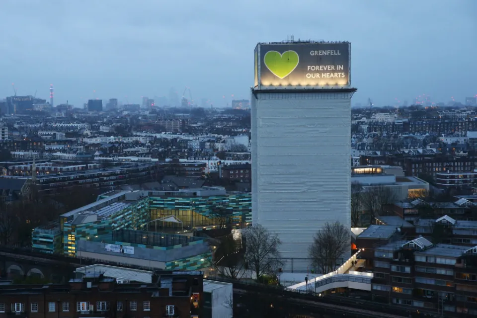 The top of grenfell tower in the evening with lights pointing up at the banner spelling out grenfell forever in our hearts