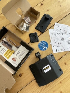 A wooden workbench shows a birdseye view of an unpacked door retainer with leaflets, instructions, screws and a product parts.