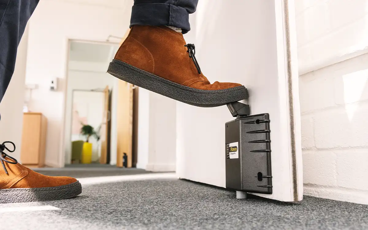 A foot pressing down the plunger of a Dorgard Pro, holding open a fire door