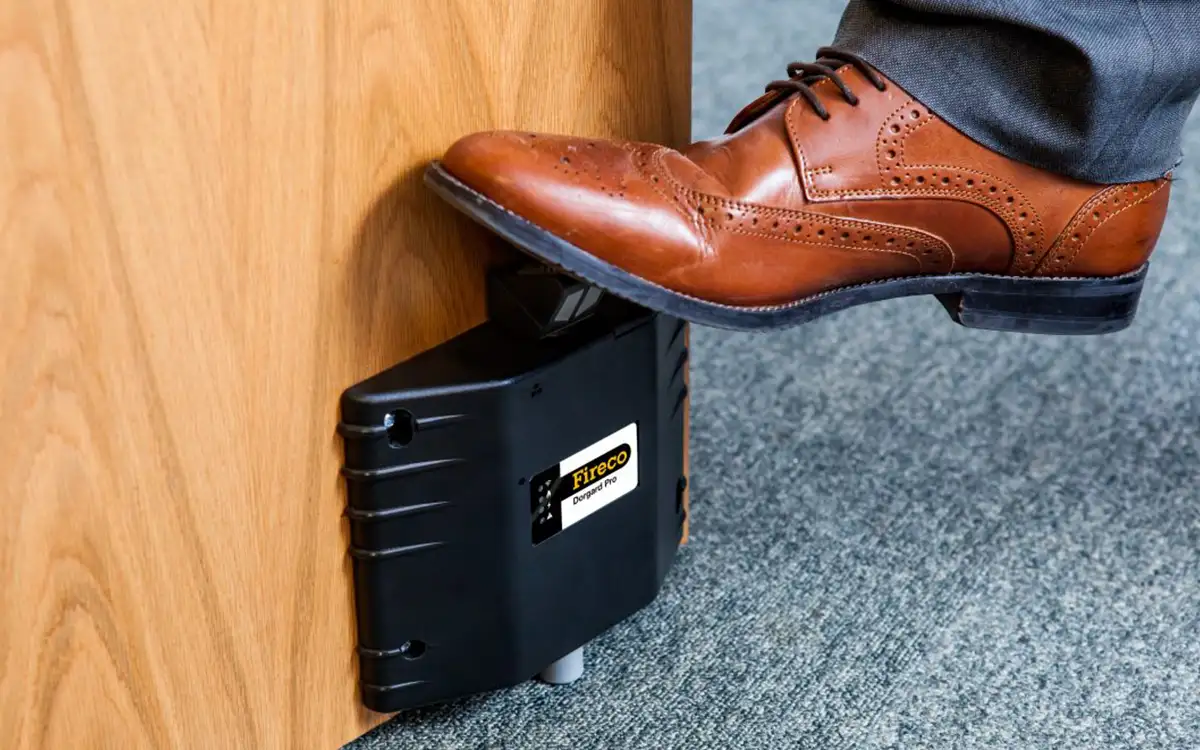 A foot pressing down to secure Dorgard Pro at the base of a fire door