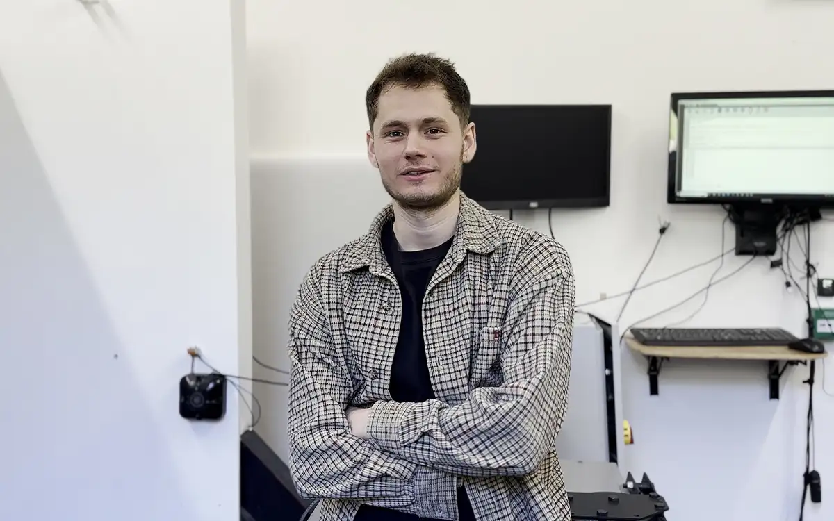 A photo of Matt, an Engineer at Fireco. His arms are crossed as he smiles at the camera. He is stood in a product test environment, with a small test unit of DorMag on the wall beside him.
