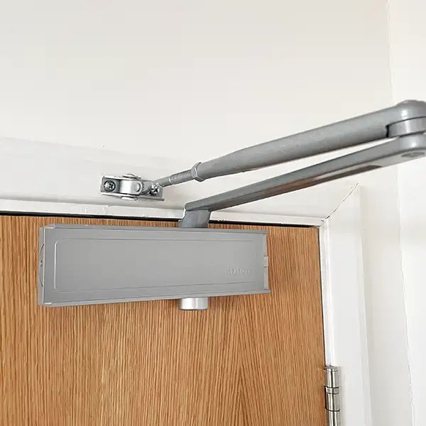 A silver closer at the topop of a fire door
