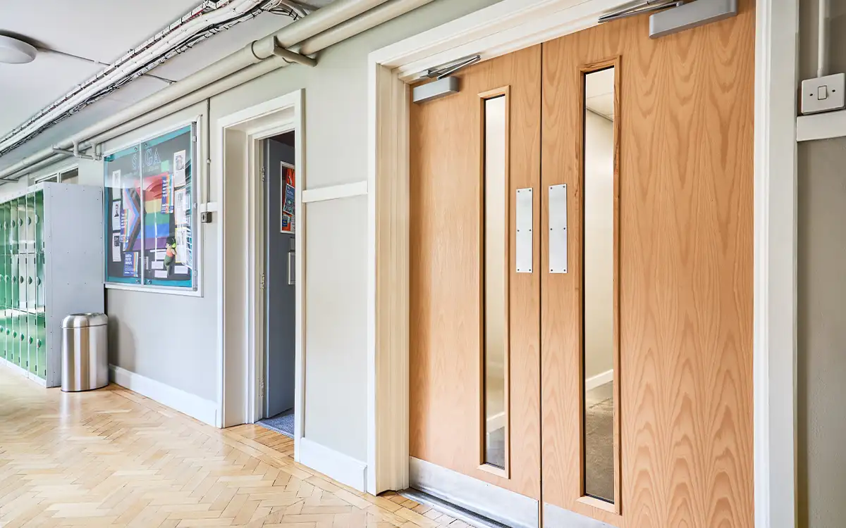 2023-05-16 DorTrak on devices_homepage cta_650z406 DorMag fire door magnet holding open a fire door in a school corridor
