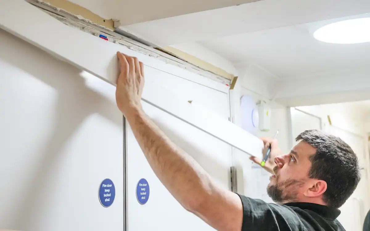 A FIreco Fire Door Installer working on the architrave around a fire door, revealing the fireproofing surrounding the door. 